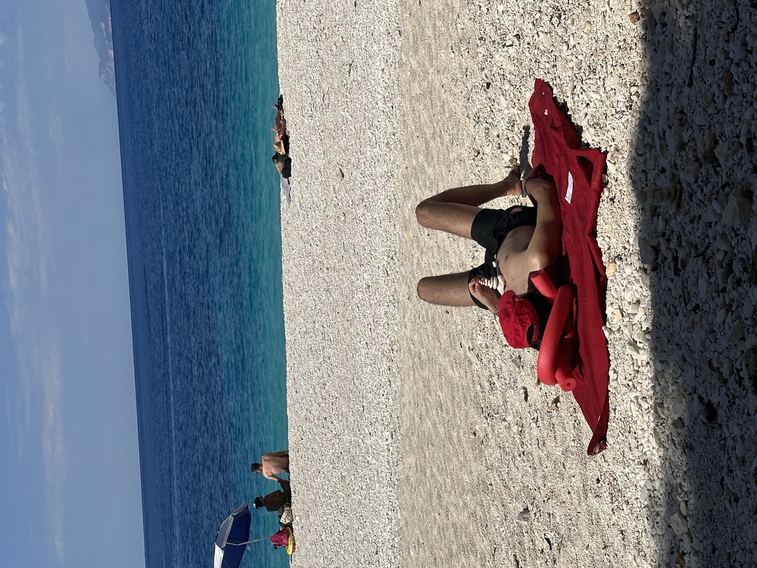 Luís on the red towel, white pebble beach